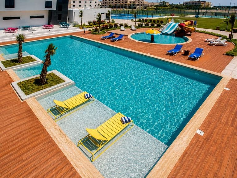 The main swimming pool, children's pool and water slides seen from above, with the padel courts beyond