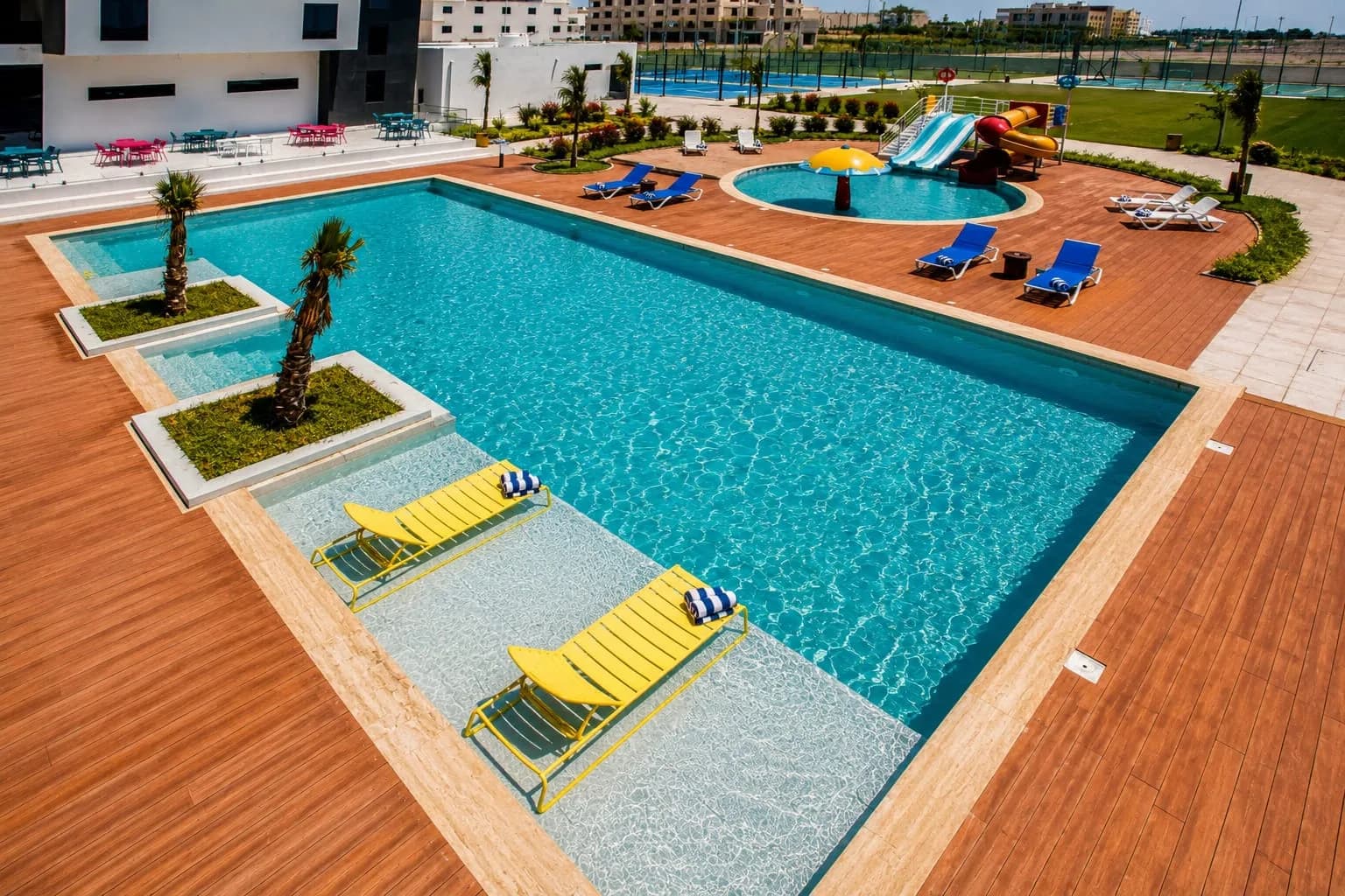 The main swimming pool, children's pool and water slides seen from above, with the padel courts beyond